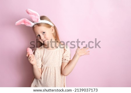 Happy Easter. A cute girl with rabbit ears holds colored eggs in her hands and smiles cheerfully. pink background. Space for text. High quality photo