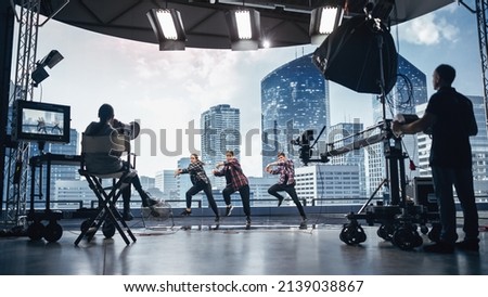Music Clip Studio Set: Shooting Hip Hop Video Dance Scene with Three Professionals Dancers Performing on Stage with Big Led Screen with Modern City Background. Director and Cameraman in Backstage. Royalty-Free Stock Photo #2139038867