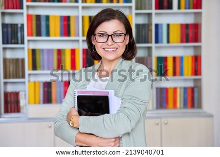 Portrait of female teacher with digital tablet textbooks looking at camera