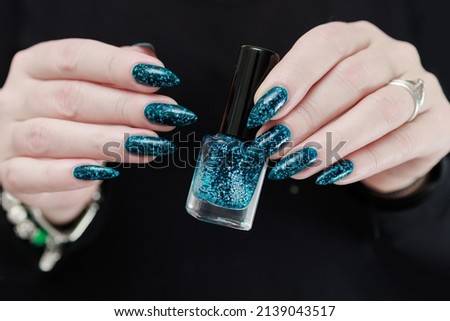 Woman hand with long nails and teal blue green manicure with bottles of nail polish