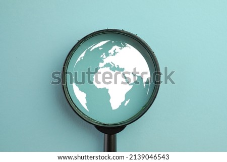 View through a magnifying glass on World icon over blue pastel background.