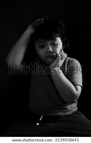 black and white portrait photo of a boy with a sad and depressed expression on a plain black background