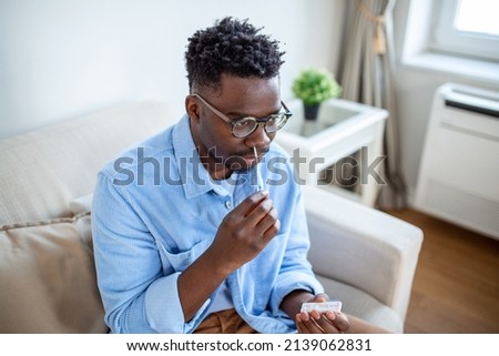 Shot of a African man using cotton swab while doing coronavirus PCR test at home. man using coronavirus rapid diagnostic test. Young man at home using a nasal swab for COVID-19.