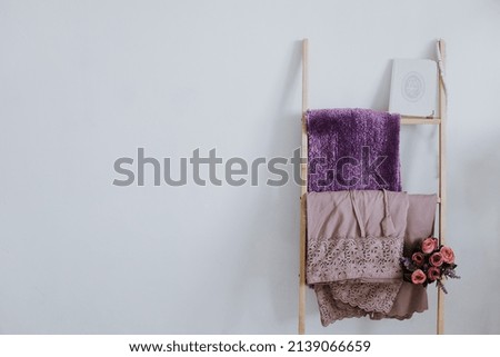 Mukena, prayer mat, tasbeeh, Al-Qur'an and purple artificial flower  on decorative ladder isolated over white background. Copy space for Ramadan Kareem, Eid al fitr, Eid al adha and Iftar concept
