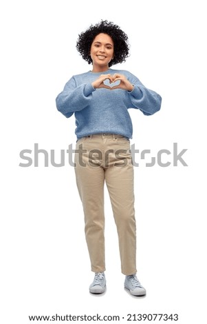 people, fashion and style concept - happy smiling woman in blue sweater and jeans showing hand heart gesture over white background
