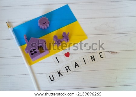 I love Ukrane. Peaceful family, toy people, home, sun, heart. Words near blue, yellow flag lay on white wooden background. Top view, flat lay, soft focus
