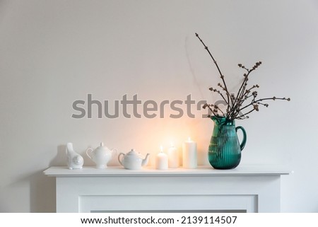 American maple branches in a green glass jar, porcelain cups, figurines, teapot on a white chest of drawers. Scandinavian style