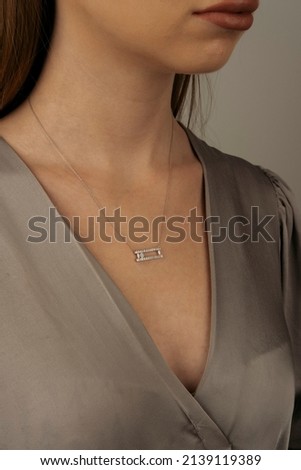 A golden necklace around the neck of a blonde-haired female model wearing a gray dress. Royalty-Free Stock Photo #2139119389