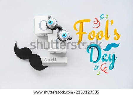 Party decor and cube calendar with date 1 APRIL on light background. April Fool's Day celebration Royalty-Free Stock Photo #2139123505