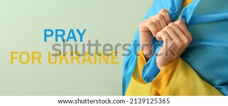 Young woman with Ukrainian flag and text PRAY FOR UKRAINE on color background