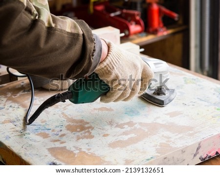 a man using a grinder removes old paint from furniture, restoration of antique furniture. handmade concept Royalty-Free Stock Photo #2139132651