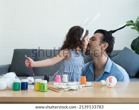 Cute little girl kisses father with love and happiness while doing art and craft activity together for Easter Holidays. 