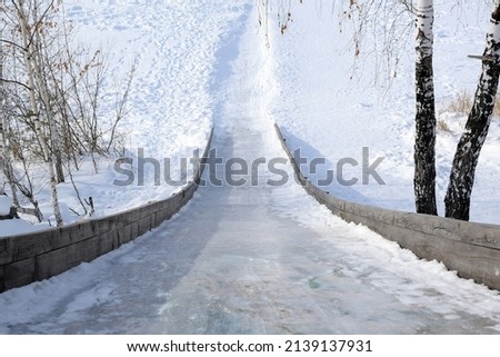 Steep descent from an icy snow slide from top to bottom. Rustic wooden slide for sledding and tubing.