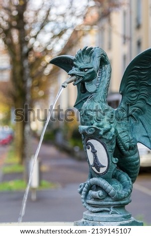 Mythical creature of basilisk on a publich water fountain with Basel city emblem of a black and white crosier, Basel, Switzerland Royalty-Free Stock Photo #2139145107