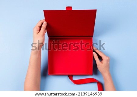 Female hands opening empty red elegant luxury box with ribbon. Mockup present gift box on light blue background. Top view Royalty-Free Stock Photo #2139146939