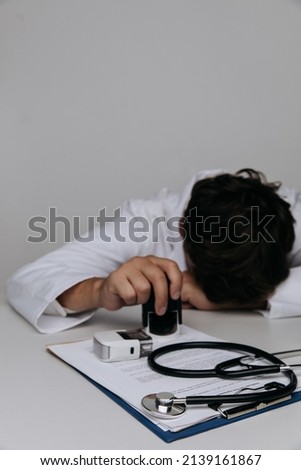 Burnout doctor feeling tired in medical office with a stethoscope on the table. Vertical image.
