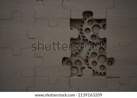 solving the problem concept - puzzles and cogwheels. wooden gears under the puzzle, the concept of moving to the next level. Cog wheels coming out from underneath a jigsaw puzzle