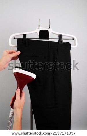 man ironing classic trousers with a steamer