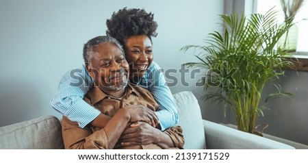 Adult daughter visits senior father in assisted living home. Portrait of a daughter holding her elderly father, sitting on a bed by a window in her father's room.  Royalty-Free Stock Photo #2139171529