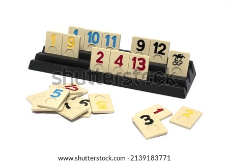 Close up of rummy game pieces with numbers and one joker partly stacked and partly on black stand game board on white background as concept for board games