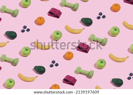 Modern minimal pattern with green dumbbells, bananas, blueberries, apples, avocado and elastic booty bands on bright pink background. Trendy female fitness aesthetic.