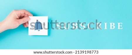 Subscripe is standing on a blue colored background, hand holds a paper with a bell symbol, social media, join and follow a blogger, newsletter buttom