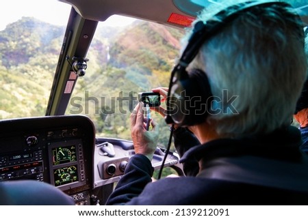 Old man filming with an action camera on the front row of a helicopter in a lush valley on Kauai island, Hawaii, United States