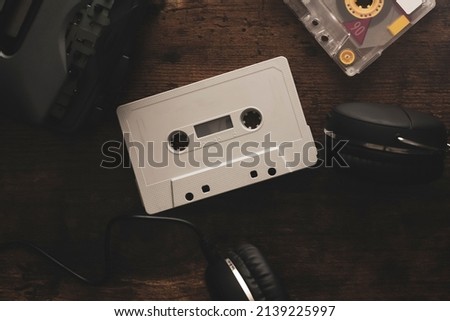 Vintage audio cassette between headphones and personal cassette player on a wood surface Royalty-Free Stock Photo #2139225997