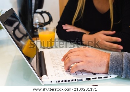 closeup of a caucasian male hand typing the keyboard of a white laptop at home, on the kitchen counter with his girlfriend