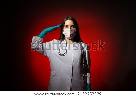 young woman doctor in a mask, with a stethoscope around her neck, white coat and gloves, salutes looking at the camera.