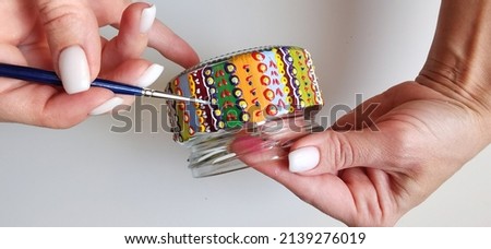 A woman holds a jar in her hands. Spot painting on glass, workshop. Drawing lesson for children in peacetime. Decorates the jar. Multicolored stained glass paints.Ideas for the decoration of objects.  Royalty-Free Stock Photo #2139276019
