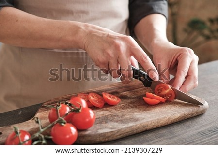 Close-up of female hands slicing cherry tomato with knife on wooden board, cooking vegetable salad Royalty-Free Stock Photo #2139307229