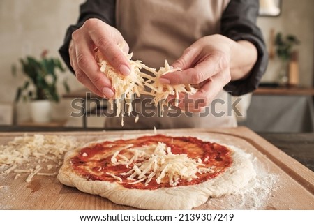 Close-up of unrecognizable woman standing at wooden board and sprinkling cheese on pizza dough with tomato sauce Royalty-Free Stock Photo #2139307249