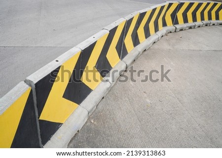 The road divider is made of cement concrete with a pattern of yellow and black stripes in the form of guide angles