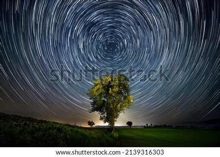 Night sky over lone tree with circular star trails, centered and symmetrical composition Royalty-Free Stock Photo #2139316303