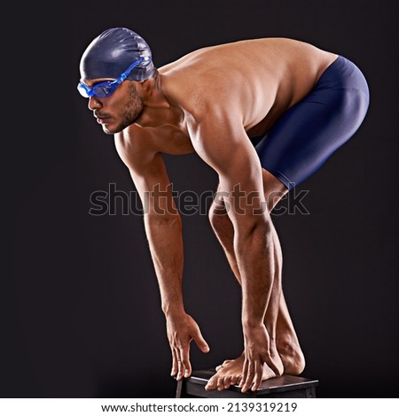 Train insane or remain the same. Studio shot of a handsome swimmer ready to dive off the starting block. Royalty-Free Stock Photo #2139319219