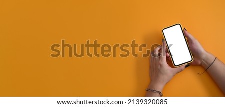 Above view woman ands holding smart phone on yellow background with copy space.
