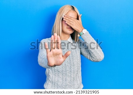 Beautiful blonde woman wearing glasses covering eyes with hands and doing stop gesture with sad and fear expression. embarrassed and negative concept. 