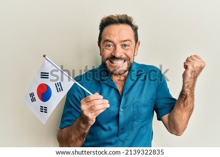 Middle age man holding south korea flag screaming proud, celebrating victory and success very excited with raised arm 