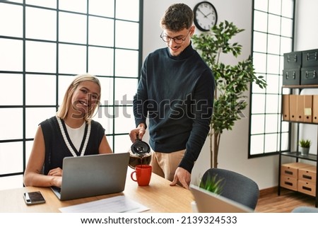 Two business workers smiling happy working and drinking coffee at the office.