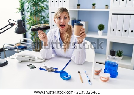 Beautiful dentist woman holding denture and toothbrush celebrating crazy and amazed for success with open eyes screaming excited. 