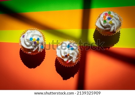 Cupcakes prepared for birthday party placed on colorful background, harshly lit by the sun and separated by crossed window shadows.