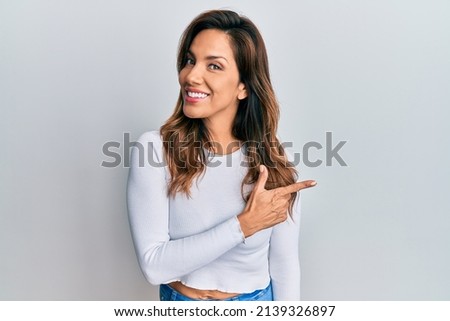 Young latin woman wearing casual clothes smiling cheerful pointing with hand and finger up to the side 