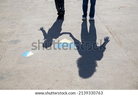 contrasting shadows of a woman and a child near a yellow-blue heart drawn with crayons on the pavement. Ukrainians want peace. Childhood during the war in Ukraine Royalty-Free Stock Photo #2139330763