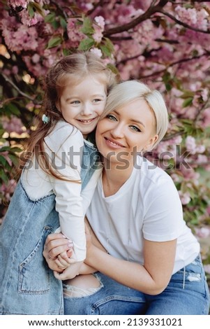 Family (mother and children) in spring city street with pink japanese cherry trees blossom (Uzhhorod City, Ukraine). Young mother with her child have fun in the park near the sakura.