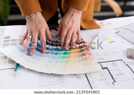 Close-up of architect woman choosing samples of wall paint. Interior designer looking at color swatch for creating project. House renovation, color palettes, architecture and interior design concept.