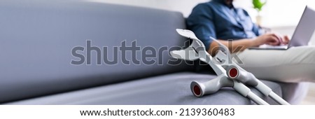 Injured Man With Broken Leg And Crutches Using Laptop Royalty-Free Stock Photo #2139360483