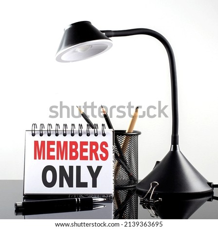 MEMBERS ONLY text on notebook with pen and table lamp on black background