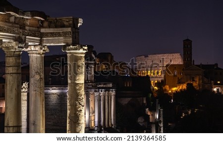 A picture of the Temple of Saturn and the Colosseum at night.