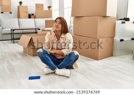 Senior middle east woman sitting on the floor at new home serious face thinking about question with hand on chin, thoughtful about confusing idea 